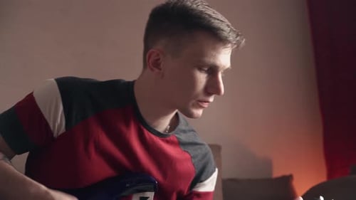 young man is learning to play the electric guitar online using a laptop. quarantine. close-up.