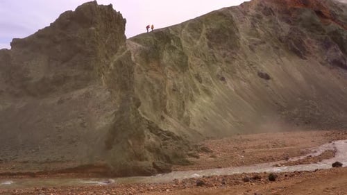 Silhouette of people climbing Bláhnúkur mountain in Landmannalaugar, Iceland, with a river and green