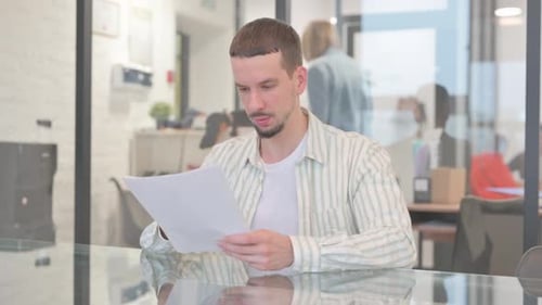 Young Man Reviewing Paperwork in Office Setting