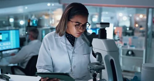 Female Scientist Using Microscope and Tablet in Lab
