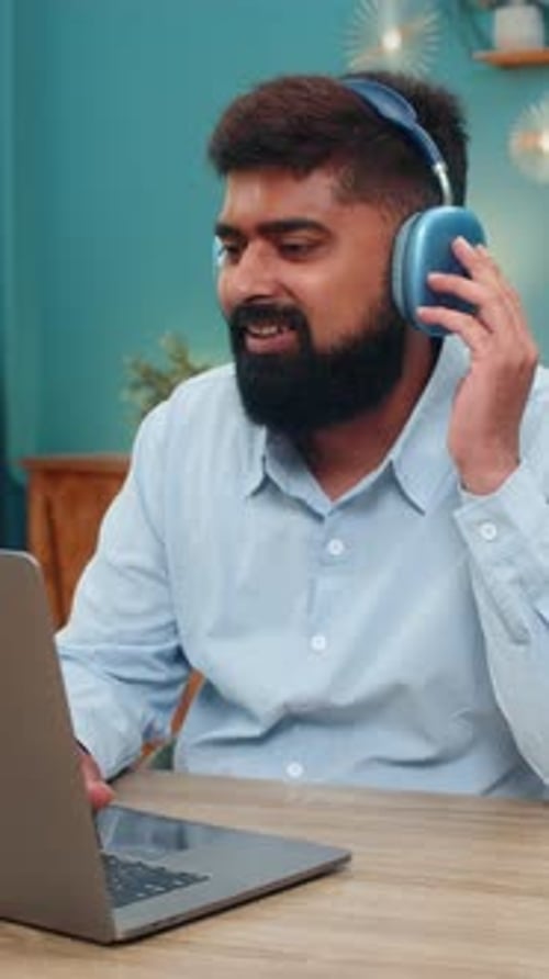 Indian Man Wearing Headphones Works on Laptop Enjoys Music Nodding Rhythm Focused Productive Indoors