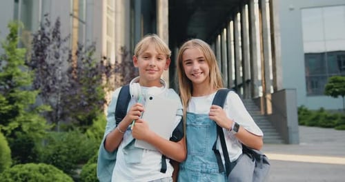 Retrato de dos hermosos niños y niñas de primaria de pie cerca del edificio de la escuela, posando