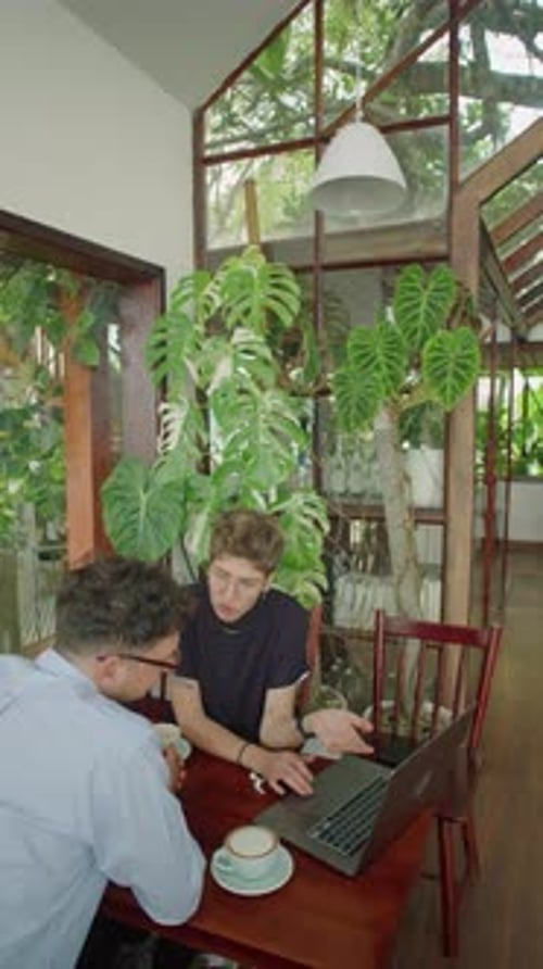 Colleagues Discussing Project on Laptop on Coffee Break in Outdoor Cafe