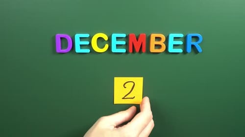 Hand sticking a sticker 2 December calendar day on school board. 2 date of December. Second day