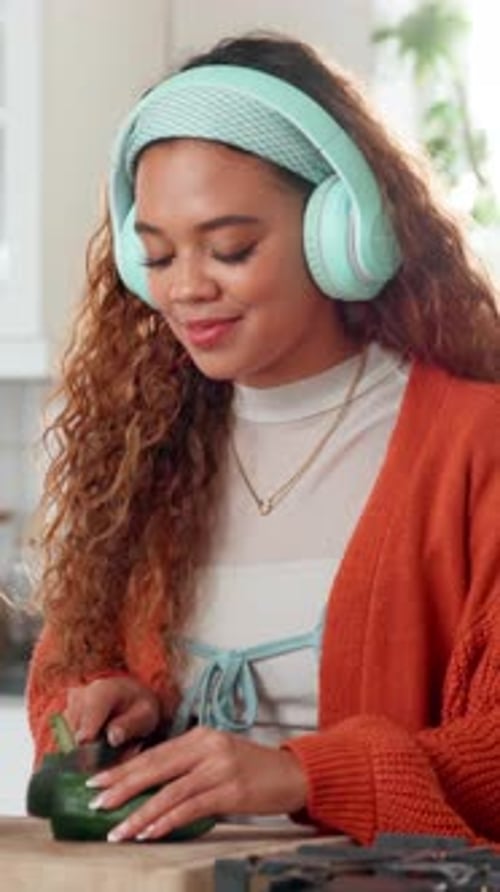 Woman with Headphones Slicing Cucumber in Kitchen