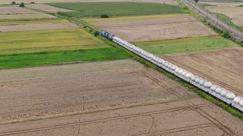Cargo train with silo wagons moves through fields in rural Poland Europe, aerial
