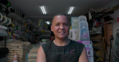 Hispanic man standing inside hardware store looking slightly aside, calm confidence, authentic work