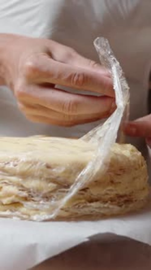 Vertical video. The pastry chef removes the plastic wrap from the Napoleon cake base.