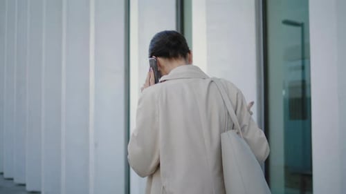 Confident businesswoman calling on phone walking near modern office building