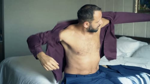 Man Dresses in Shirt while Sitting on Bed