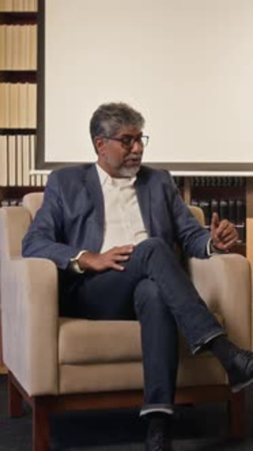 Man in Blazer Speaking While Sitting in Chair