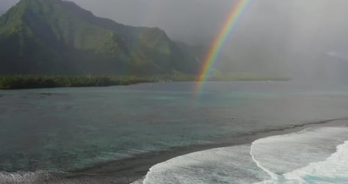 Arc-en-ciel sur une baie tropicale brumeuse et des sommets de montagnes verdoyants