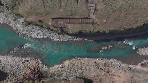 Blue glacial river in Stuðlagil canyon with tourist viewing platform on cliff, aerial