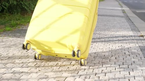Yellow Suitcase Rolling on Cobblestone Sidewalk