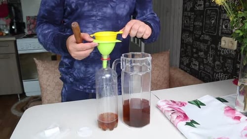 Um homem derrama vodka com infusão de lavanda de um decantador em uma garrafa. Usa um funil e uma peneira