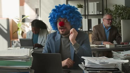 Portrait of Businessman in Clown Wig and Nose Working at Desk in Office