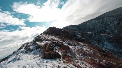 A snow-capped mountain ridge on a partly cloudy day, aerial view
