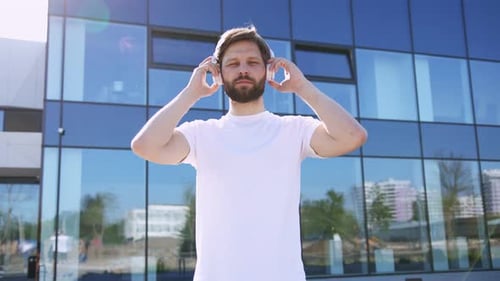 Young Man Puts on Headphones Outside Urban Building