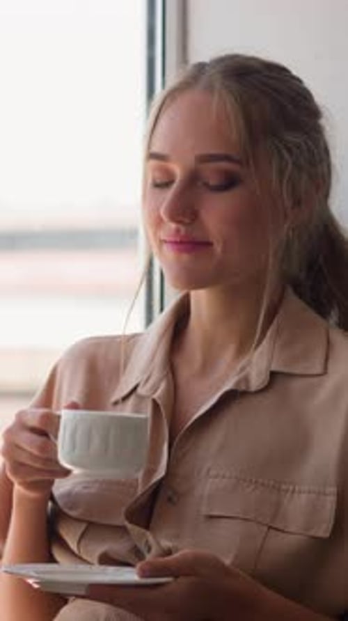 Pensive Woman Sits on Windowsill Having Cup of Hot Drink