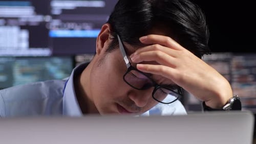 Primer plano del programador que tiene dolor de cabeza mientras escribe código con una computadora portátil usando varios monitores