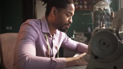 Male fashion tailor working on the sewing machine for the suit design in his workshop.