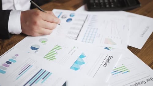Close Up of a Businessman Hands with Pen Working at Office Desk and Analyzing Graphs and Charts and