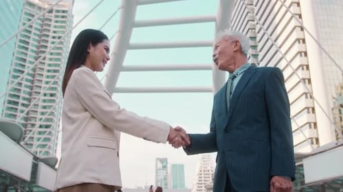 Asian senior mature middle aged businessman handshaking young businesswoman in modern city