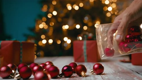 Hand empties Christmas Ornaments onto Table near Gifts