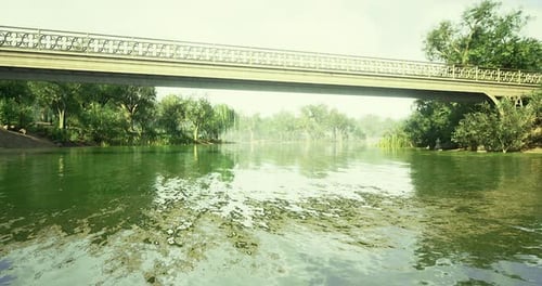 Blick auf einen ruhigen Fluss, der unter einer dekorativen Brücke in einer üppigen Landschaft fließt