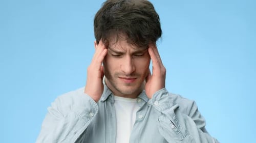 Man Holds Head and Shows Signs of Discomfort in a Plain Background During a Health Awareness Segment