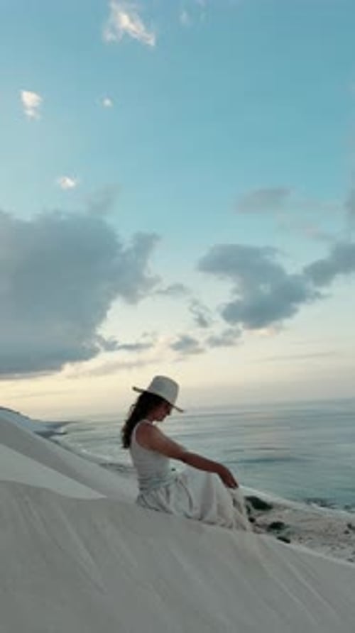 Woman in White Dress Sits on Sandy Ocean Dune