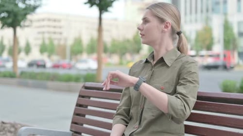 Young Woman Checks Smart Watch on City Bench