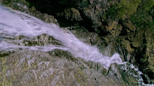 Ascending top down shot of cascading waterfall crashing down rocky mountains