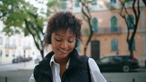 Relaxed african american woman enjoys music in wireless headphones on city street