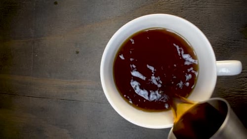 Top view of coffee being poured in to white mug with circling bubbles and steam