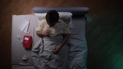Man Lying in Bed Taking Pill with Water