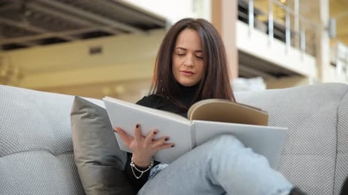 Woman Sitting on Sofa and Reading Catalog Inside Furniture Store