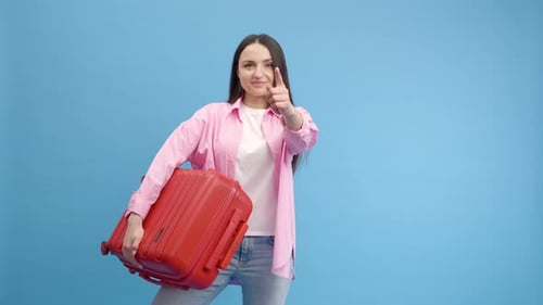 Smiling woman doing advertisement in studio on blue background with red suitcase