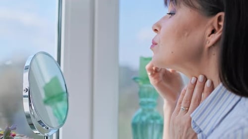Woman Applying Lotion to Her Face in Mirror