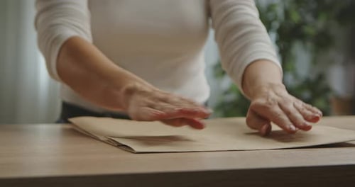 Una mujer doblando a mano una bolsa de papel artesanal sobre una mesa de madera