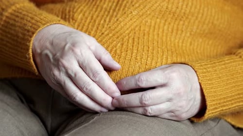 Senior Hands Clasped Wearing an Orange Sweater