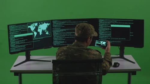 Soldat asiatique travaillant avec un téléphone portable tout en écrivant du code avec plusieurs écrans en vert