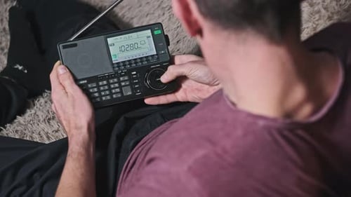 Man Turning Modern Portable Radio With Digital LCD Frequency Scale on Home Couch