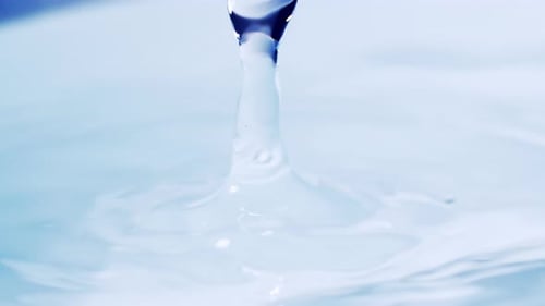 Close up real of water drop falls into water and diverging circles of water with smoot color backgro