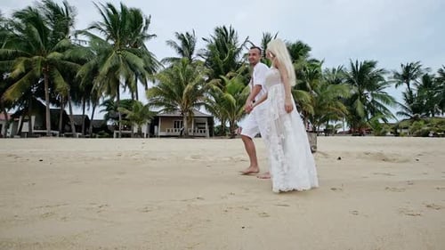 Couple in White Strolling Along Sandy Beach