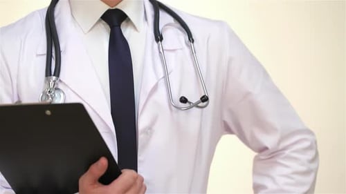 Selbstbewusster Arzt hält die Zwischenablage in der Hand und posiert vor einem sauberen weißen Hintergrund