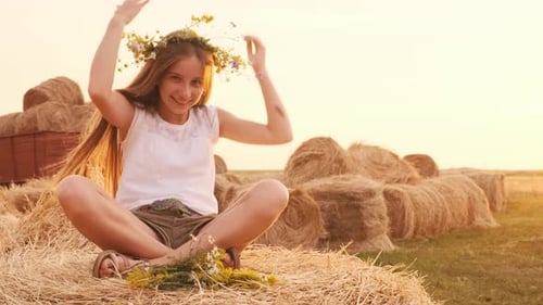 Girl Adjusts Flower Crown Sitting on Hay Bale