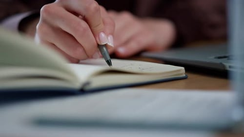 Woman writing in notebook at desk with laptop