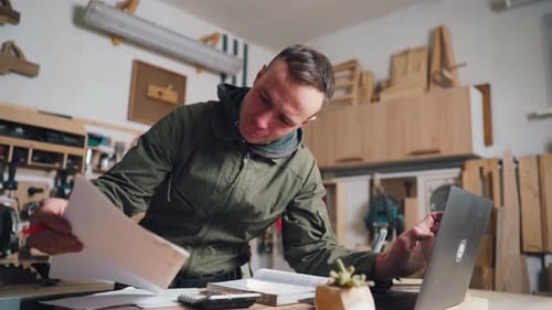 The Carpenter Works with Documents for a New Furniture Order in His Own Workshop
