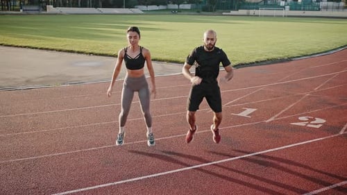 Young Man and Woman Squat with Jumping on Stadium in Morning